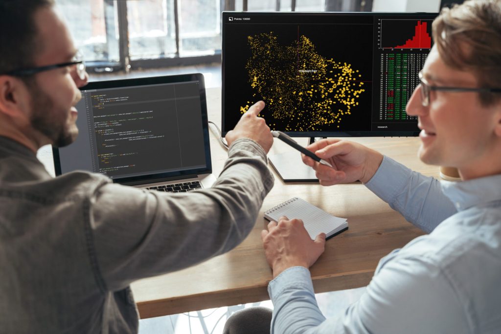 Nahaufnahme von zwei Spezialisten für maschinelles Lernen, die in einem Büro vor einem PC über ein neues Projekt diskutieren und Daten analysieren. Selektive Fokussierung auf den Bildschirm des Computers.