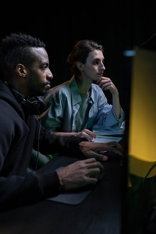 Ein schwarzer Mann und eine europäische Frau arbeiten an einem Computer, konzentriert und kooperativ, vor einem modernen, eleganten Arbeitsplatz-Hintergrund.